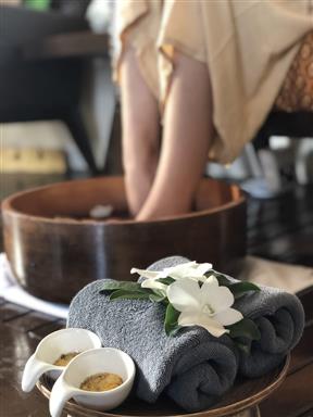 Serviettes roulées, fleur blanche et bols de soin devant un bain de pieds